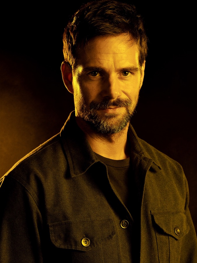 Bearded tradesman lit by a warm gold key light against a dark background